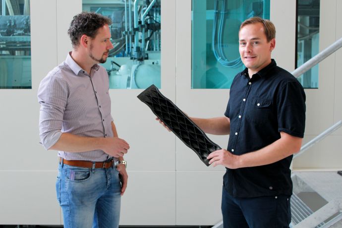Norbert Schramm (rechts im Bild) präsentiert einen vom MERGE-Team entwickelten Seitenaufprallträger in Leichtbauweise. Die angespritzte Rippenstruktur erhöht dessen Steifigkeit.